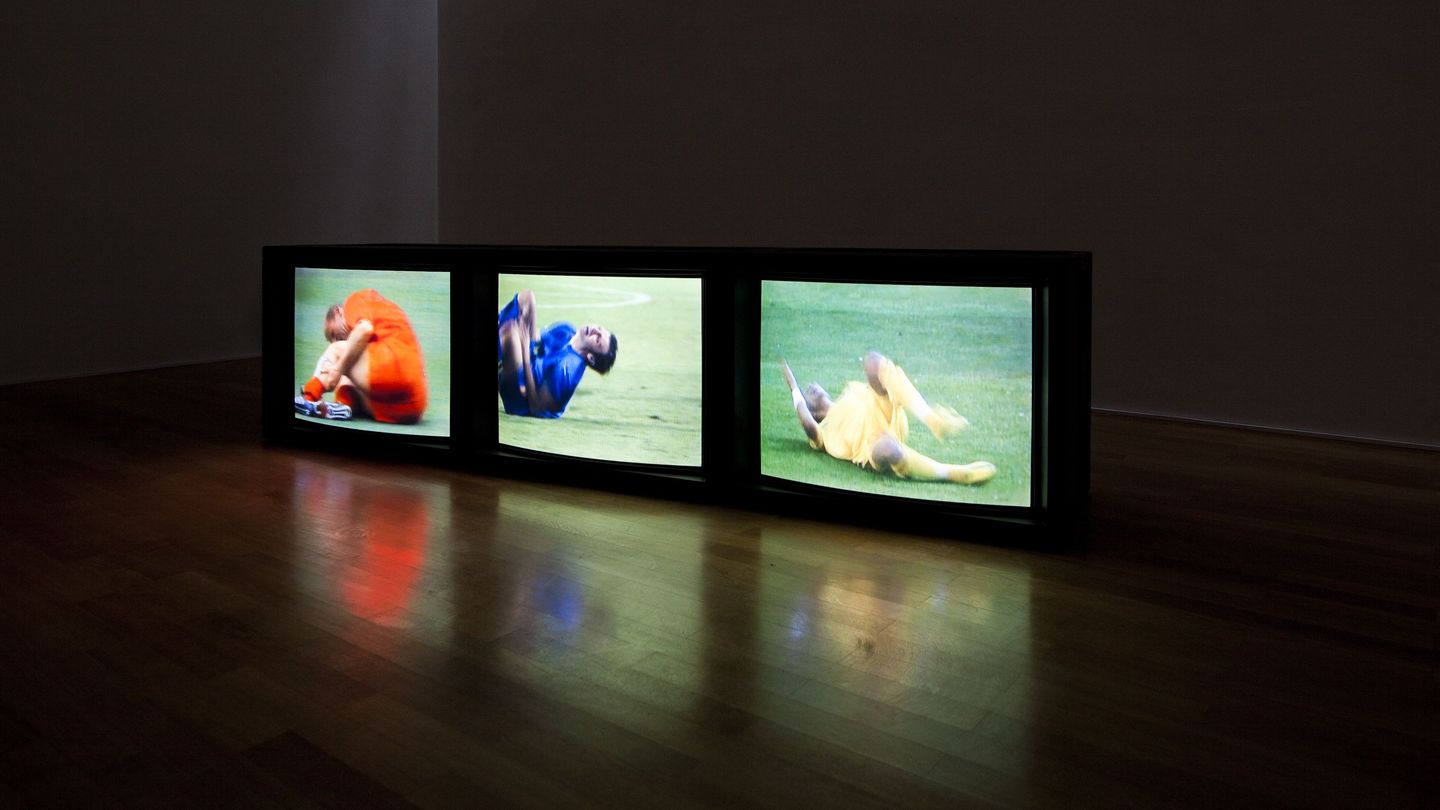 Video installation of three monitors lined up side by side on the floor, all three showing different scenes of falling soccer players in close-up. Paul Pfeiffer, Sammlung Goetz Munich