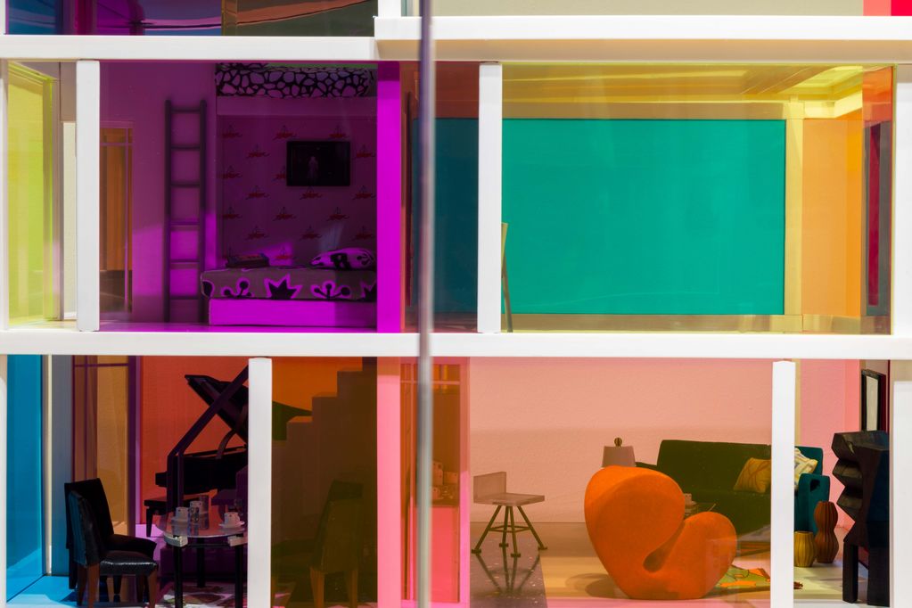 Blick in ein Puppenhaus durch bunte Plexiglas-Fenster. Im Innenraum sind Designmöbel und ein Flügel zu erkennen