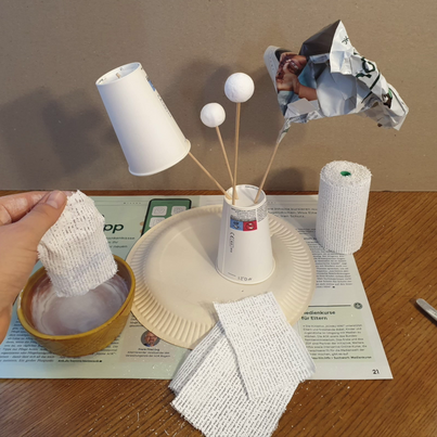 Eine Skulptur aus Pappbechern und Zeitungspapier wird mit Gipsbandagen abgedeckt