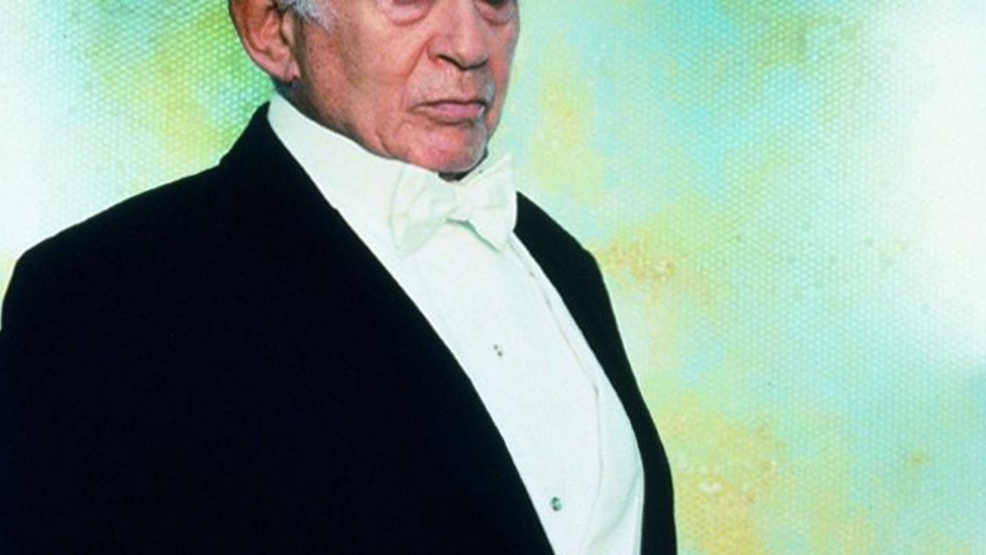 This shot shows a portrait of the Harry Houdini character from the Cremaster cycle by the artist Matthew Barney. He wears a tuxedo with a white bow tie and looks directly into the camera in three-quarter profile. 