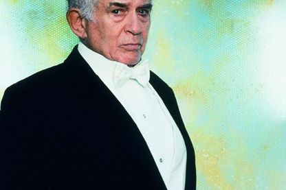 This shot shows a portrait of the Harry Houdini character from the Cremaster cycle by the artist Matthew Barney. He wears a tuxedo with a white bow tie and looks directly into the camera in three-quarter profile. 