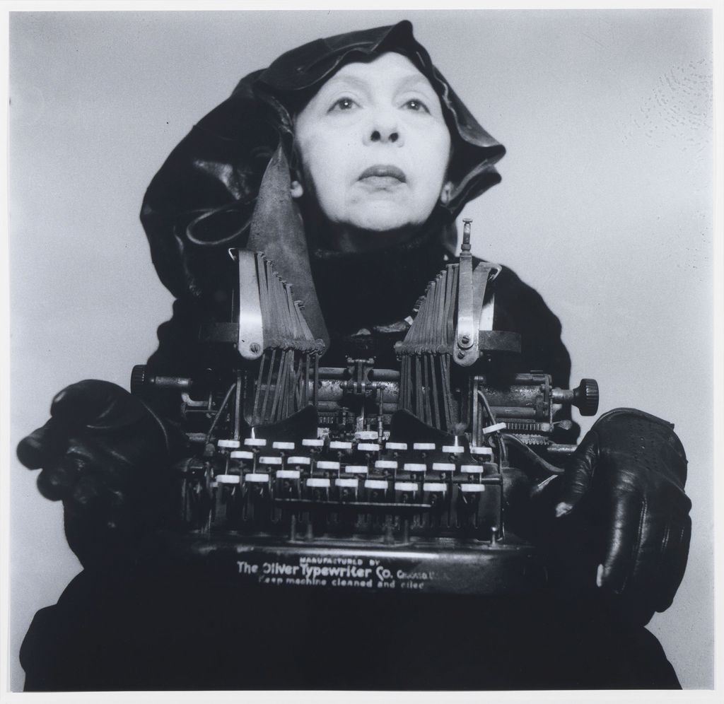 Black and white photograph of an elderly woman in a black frock holding a typewriter in her hands. Geta Brătescu, Sammlung Goetz Munich