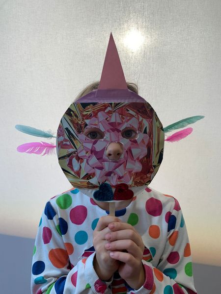 Child with dotted top holds homemade mask in front of face