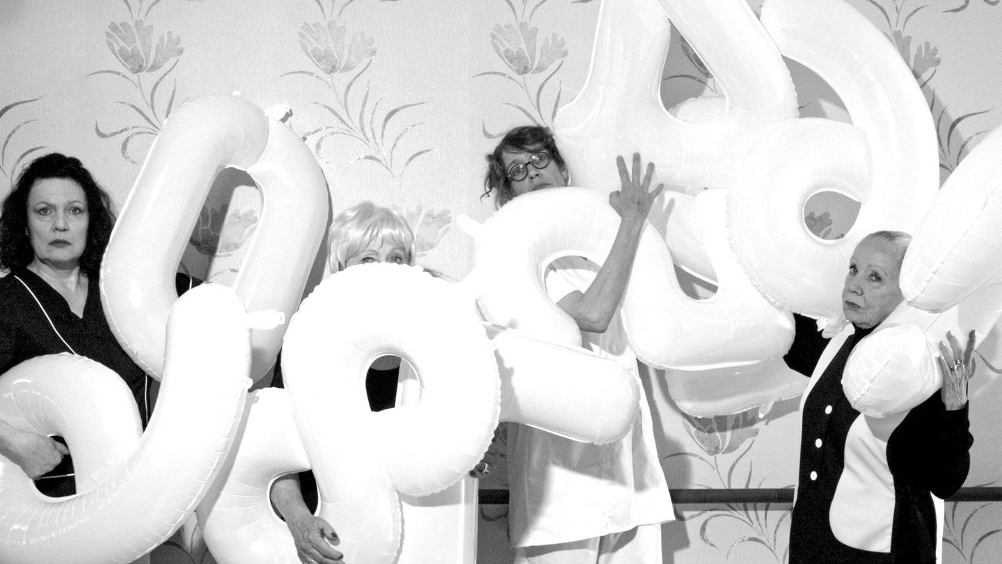 Black and white photograph of four women holding number balloons