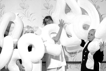 Schwarzweißfotografie von vier Frauen mit Zahlen-Luftballons