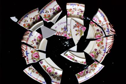 Video Still, das einen zersprungenen Teller auf schwarzem Grund zeigt, den ursprünglich ein Blumenrand und der Spruch "Republica de Colombia para siempre" zierte. Juan Manuel Echavarria, Sammlung Goetz München