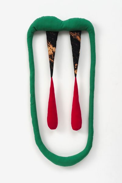 A green, padded fabric strip forms an oval, mouth-like shape. From the upper strip, which curves slightly like lips, additional filled fabric strips hang down, their tips tinted red and reminiscent of fangs.