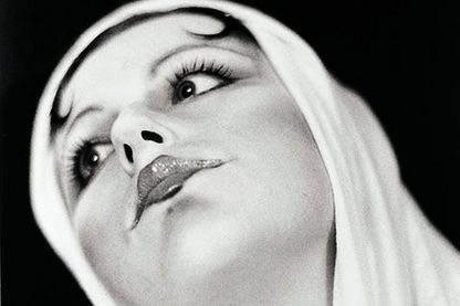 Schwarzweißfotografie des Gesichts und Halses einer Frau, die stark geschminkt ist und ihre Ponyfransen zu Schnecken eingedreht hat, über welche sie ein helles Tuch gelegt. Cindy Sherman, Sammlung Goetz München