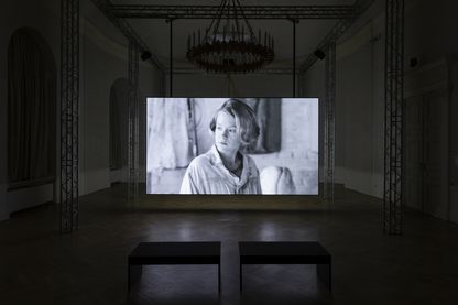 Ausstellungsraum mit großer Leinwand, auf der ein Video Still in schwarzweiß von einer jungen blonden Frau zu sehen ist. Teresa Hubbard/Alexander Birchler, Sammlung Goetz München