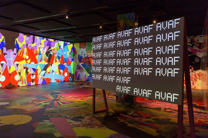 Bunt gestalteter Raum mit Tafel darin, auf der sich die Abkürzung AVAF (assume vivid astro focus) in LED-Schrift wiederholt. Sammlung Goetz München