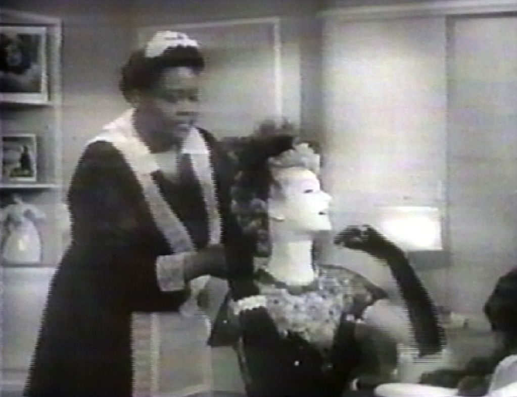 Video Still, which looks like an old recording from television. The image is black and white and blurred. It shows a black housekeeper who seems to be helping her white employee with her evening dress. Tracey Moffat/Gary Hillberg, Sammlung Goetz Munich