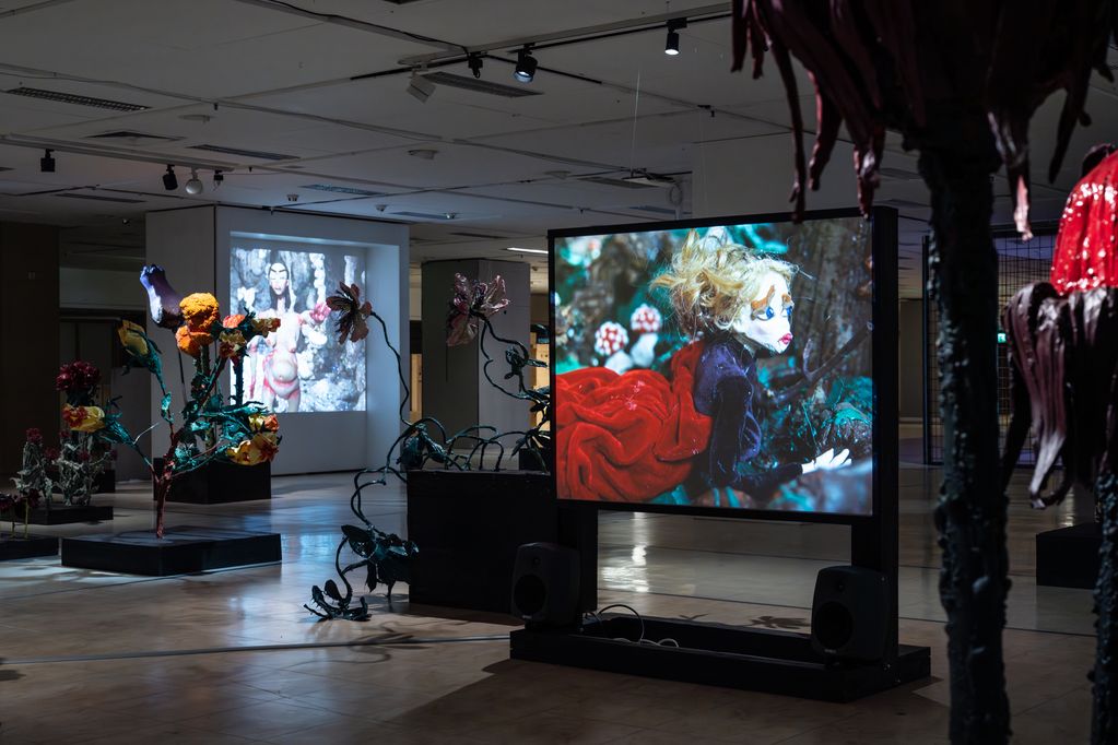 Somber walk-through installation with oversized flower sculptures and video projections