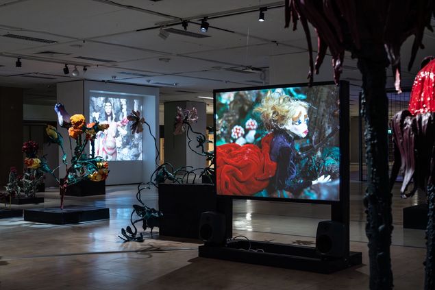 Somber walk-through installation with oversized flower sculptures and video projections