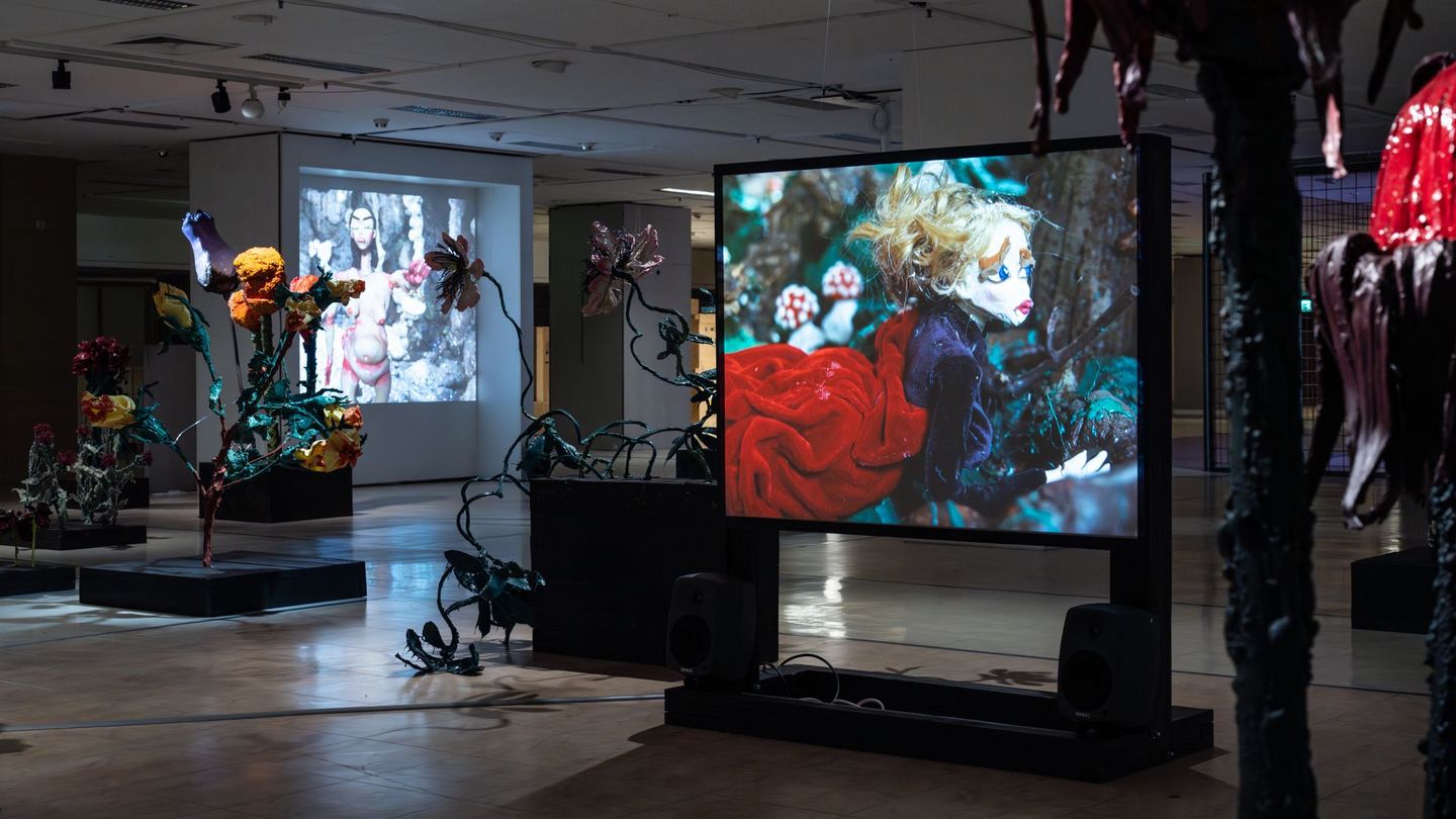 Somber walk-through installation with oversized flower sculptures and video projections