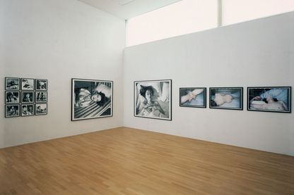 Diese Installationsansicht zeigt fotografische Arbeiten des japanischen Künstlers Nobuyoshi Araki. An der linken Wand hängen neun kleinere Formate in Dreierreihen, bestehend aus Schwarzweißfotografien frivoler, japanischer Mädchen in Schuluniform. Rechts daneben hängt eine großformatige Schwarzweißfotografie einer gefesselten Frau mit entblößtem Oberkörper. An der rechten Wand ist wieder eine großformatige Schwarzweißarbeit von einer jungen Frau, deren Kopf und Hals aus einer Bettdecke herausschauen. Daneben hängen Farbfotografien von Teilansichten nackter Frauen, deren Intimbereiche mit einem spitzen Gegenstand weg gekratzt worden sind. 