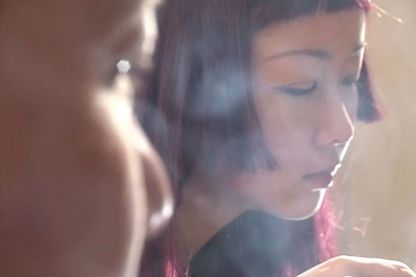 Das Gesicht einer jungen asiatischen Frau in Zigarettenrauch gehüllt