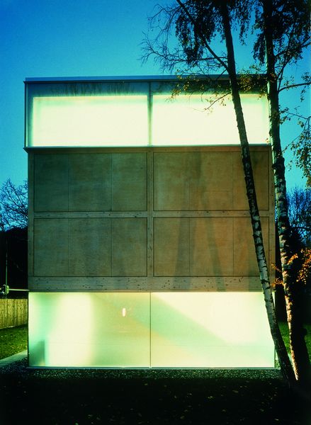 Schwarzweißfotografie der kurzen Fassadenseite des rechteckigen Ausstellungsgebäudes der Sammlung Goetz bei Abendlicht. Die Innenbeleuchtung strahlt durch die breiten Fensterbänder.