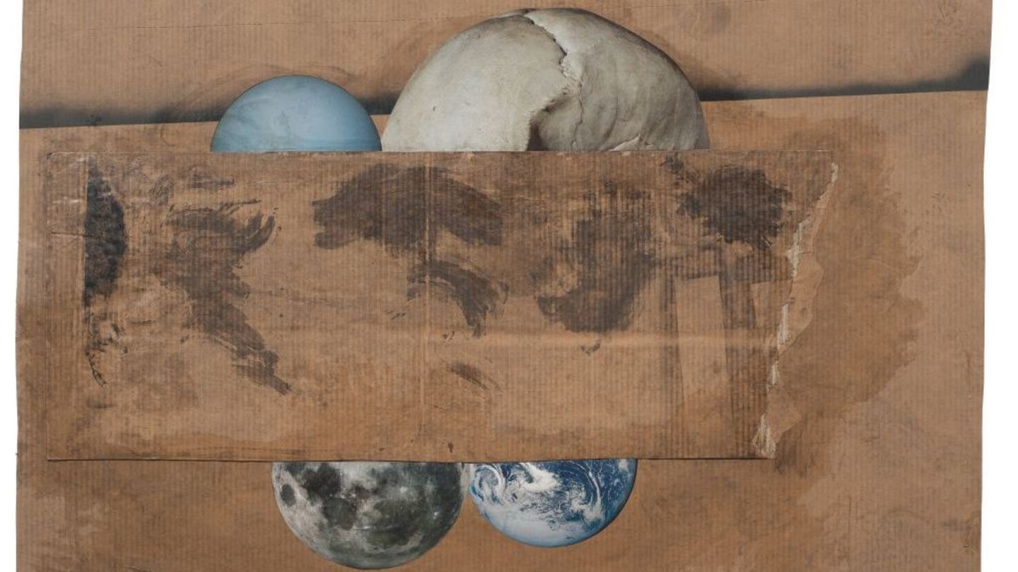 Four spherical objects including a half skull partially covered by a rectangular brown cardboard on a brown cardboard background