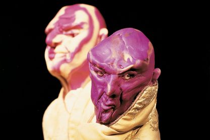 This photograph consists of a close-up of two male head sculptures. They have no hair, but an expressive facial expression. They are also dressed with high-quality fabrics. 
