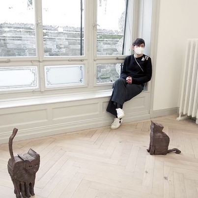 © Zilla Leutenegger Photography of the artist with mouth-nose protection. In front of her on the floor are two bronze cat sculptures. Sammlung Goetz, Munich